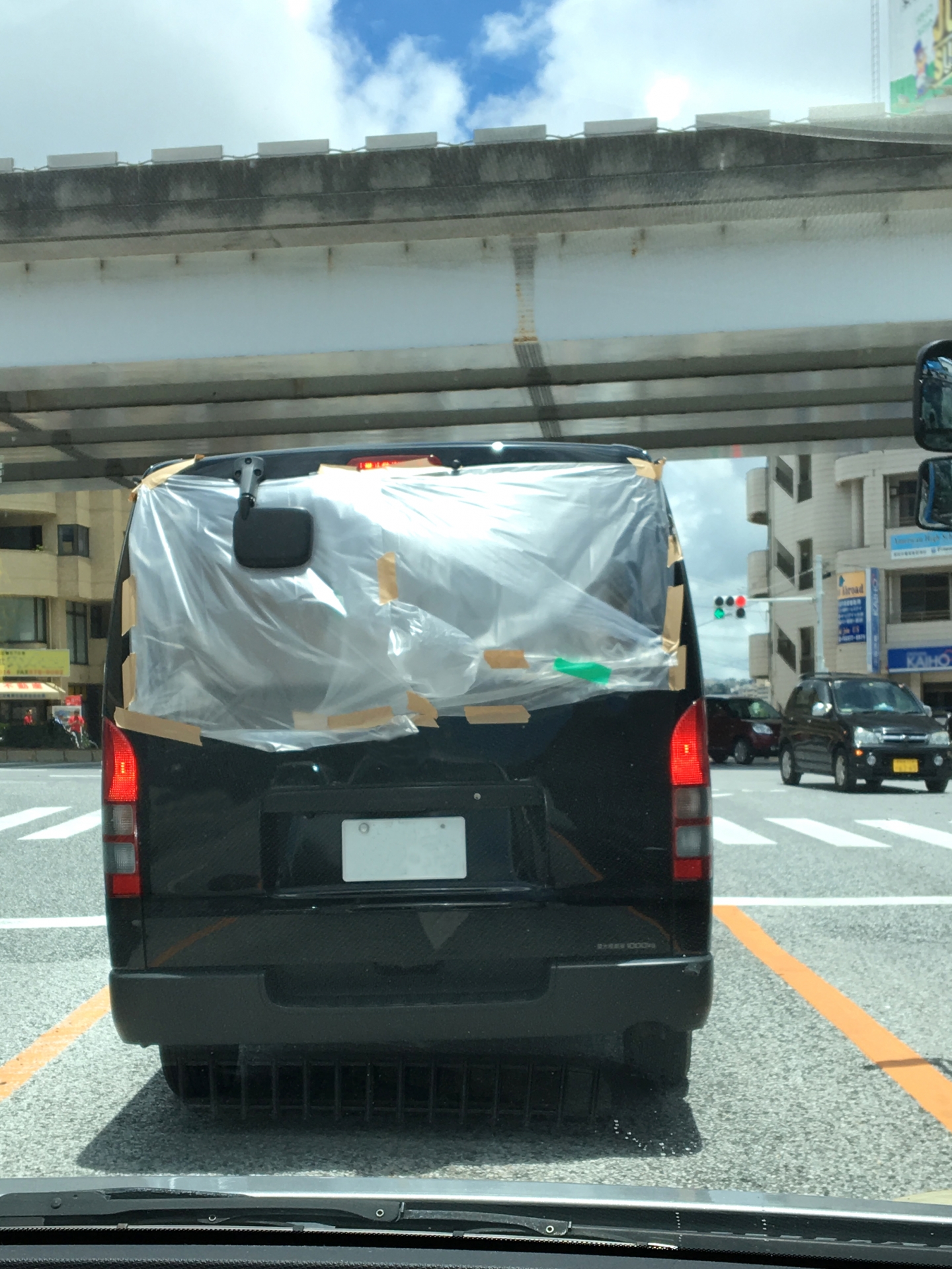 壊れたリアガラスにシートを貼って走行する車