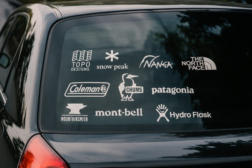 コンパクトカーのリアガラスにアウトドアブランドのシールがたくさん貼られた車