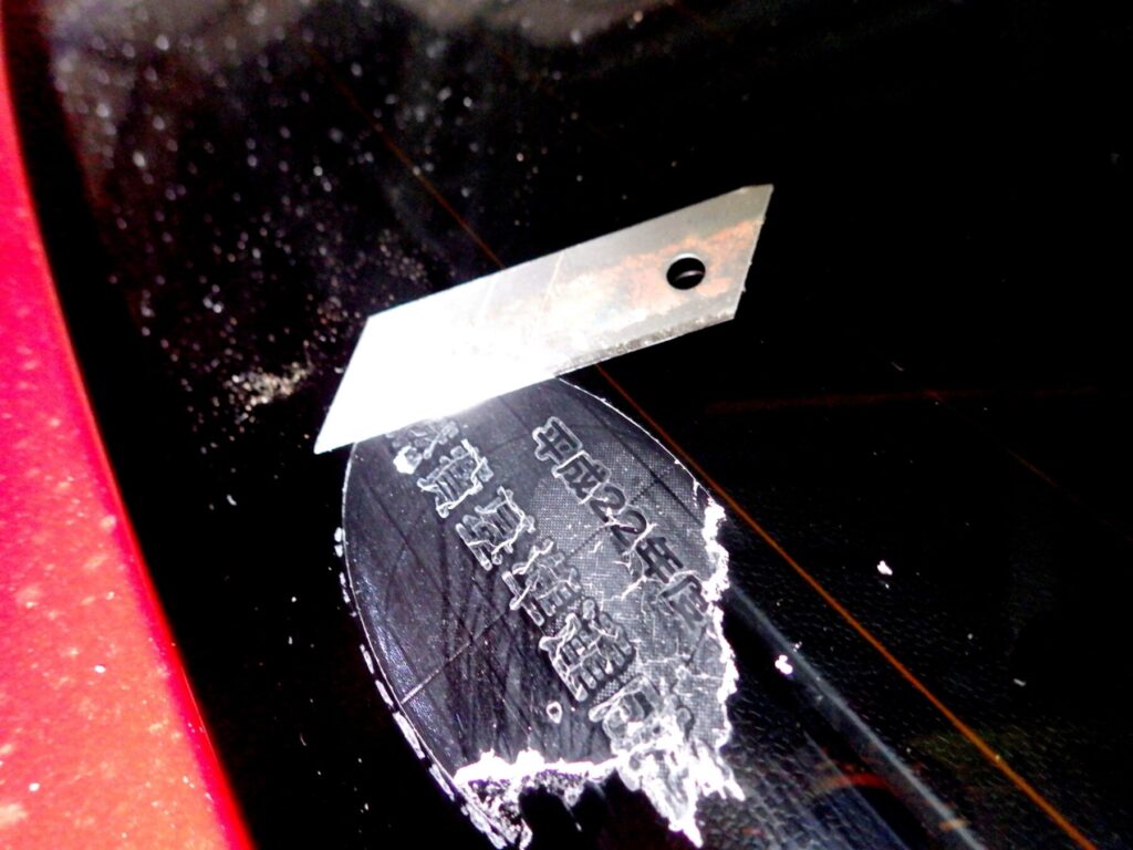 リアガラスに貼られたステッカーが硬化してカッターの刃でこすり落とす