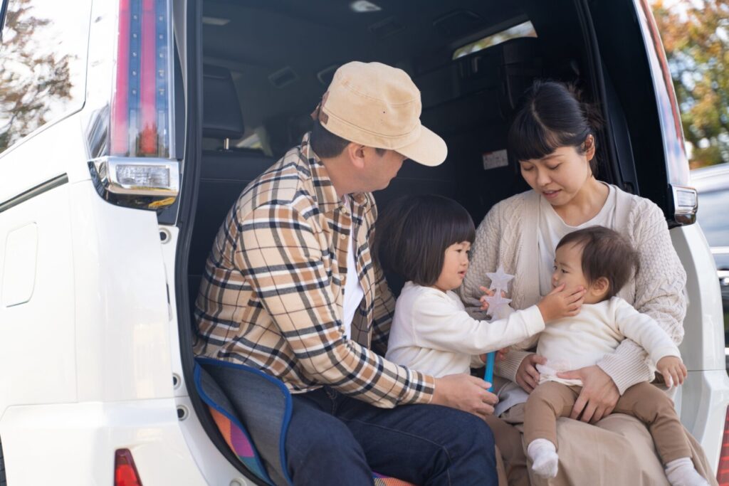 軽自動車のバックドアを開けて家族4人で座る